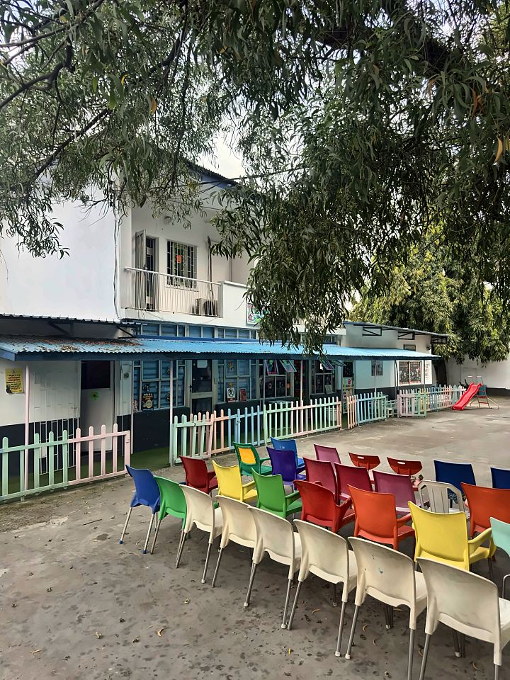Colourful chairs set out in the main courtyard, with classrooms behind pastel picket fences