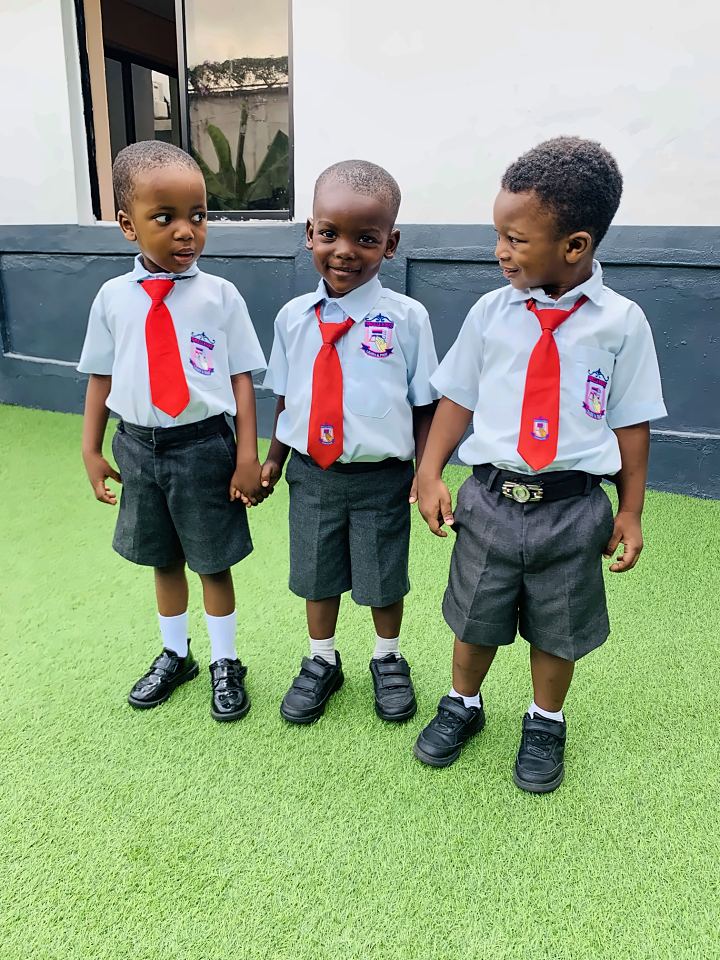Three young pupils in uniform holding hands on the school lawn